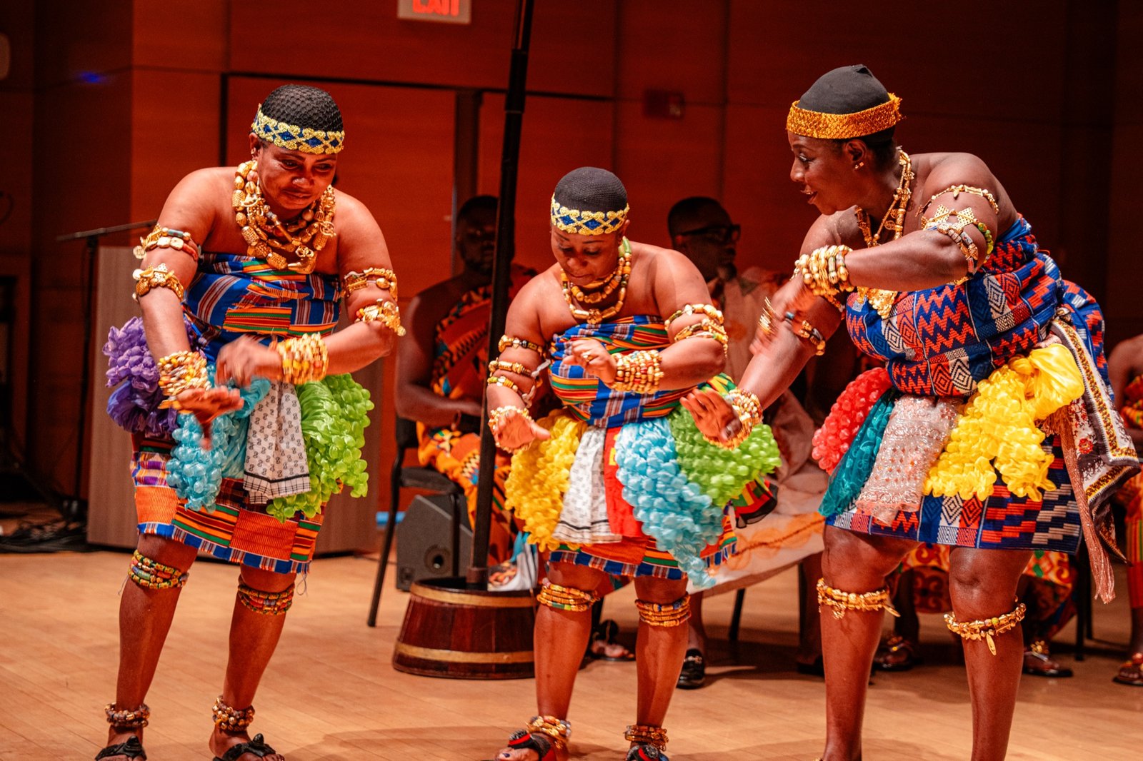 Three dancers in traditional gold and patterned costumes performing on stage