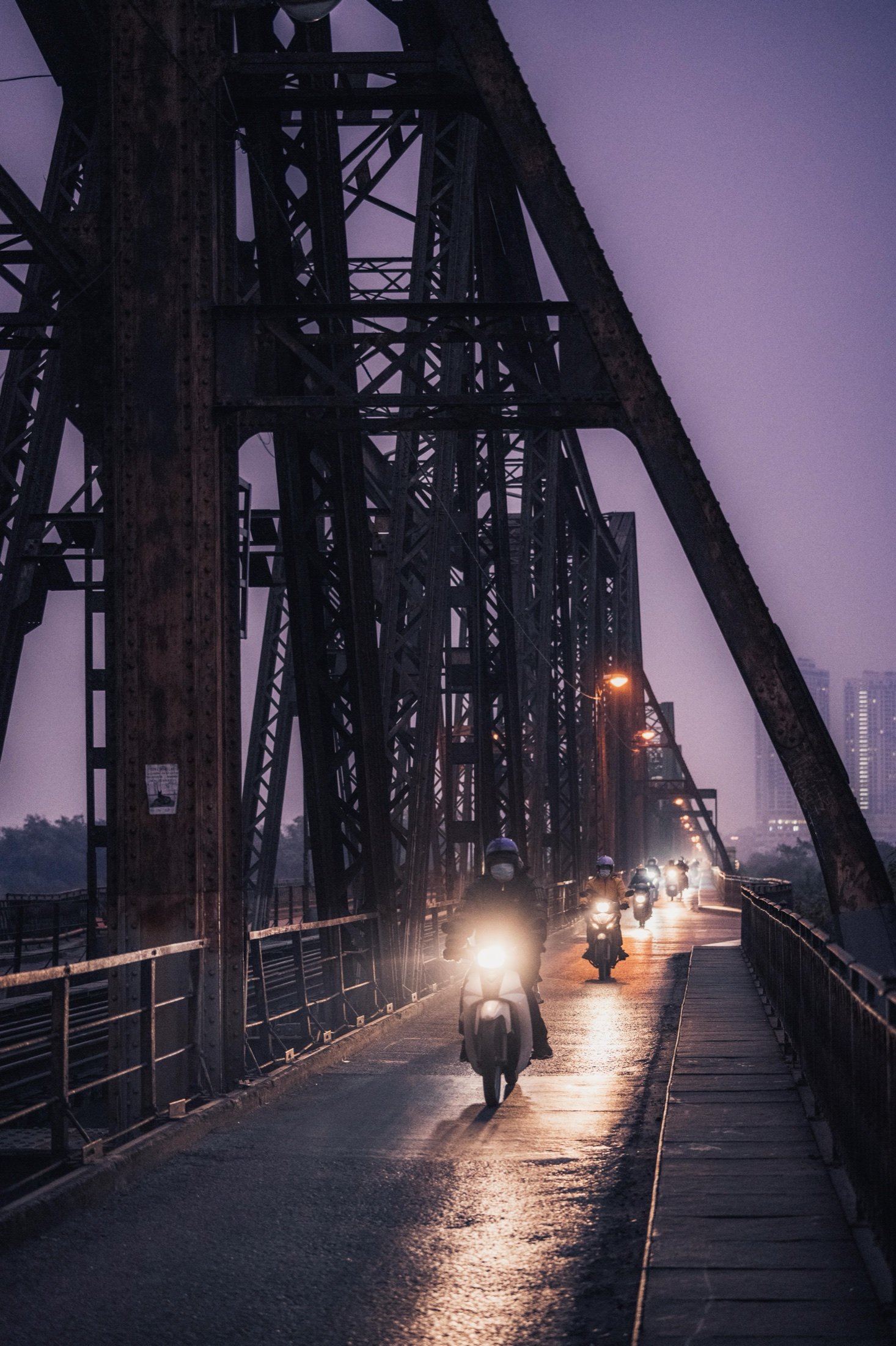 Old iron truss bridge at dusk with motorbikes riding across, purple sky