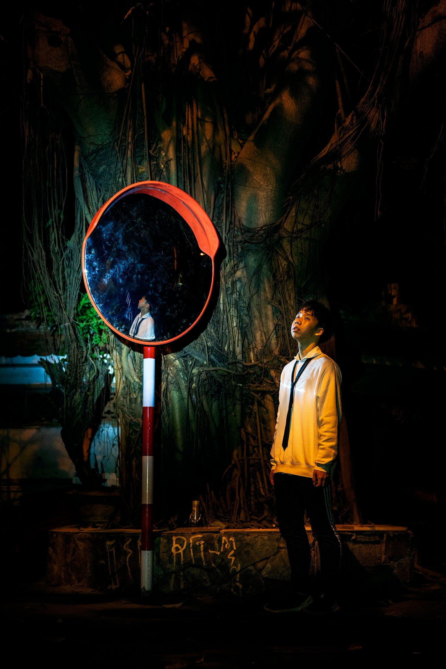 Young man looking up at a road mirror reflecting a figure, night portrait